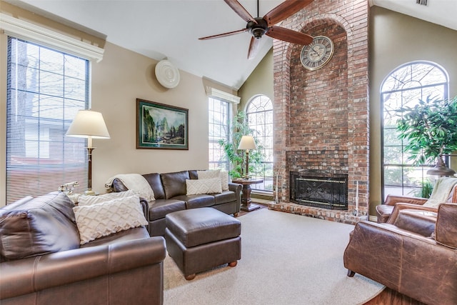 carpeted living area with a wealth of natural light, a ceiling fan, high vaulted ceiling, and a fireplace