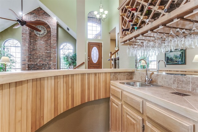 kitchen with light brown cabinetry, ceiling fan with notable chandelier, a sink, light countertops, and a towering ceiling