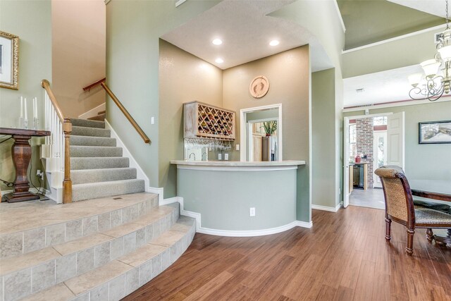 stairway featuring bar area, baseboards, a high ceiling, an inviting chandelier, and wood finished floors