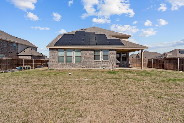 rear view of property featuring roof mounted solar panels, a lawn, and a fenced backyard