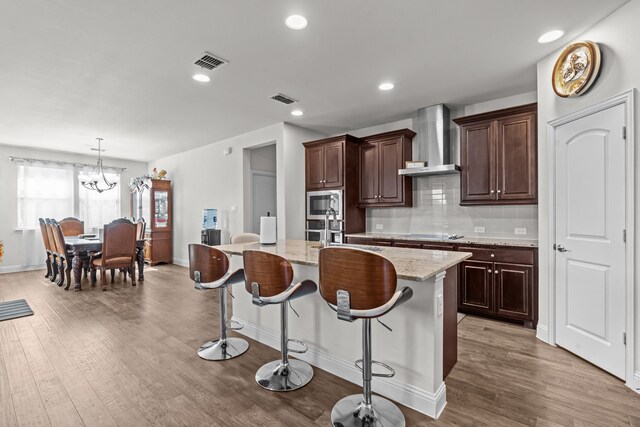 kitchen with a kitchen island with sink, stainless steel microwave, wall chimney range hood, and visible vents