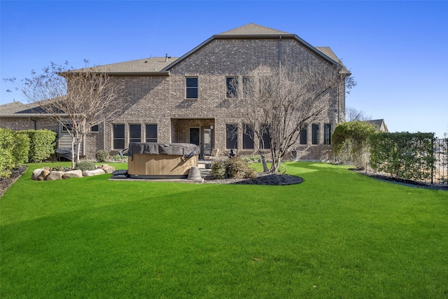 rear view of house with a yard, brick siding, and a hot tub