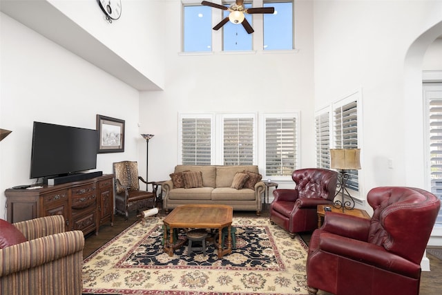 living area with arched walkways, ceiling fan, and wood finished floors