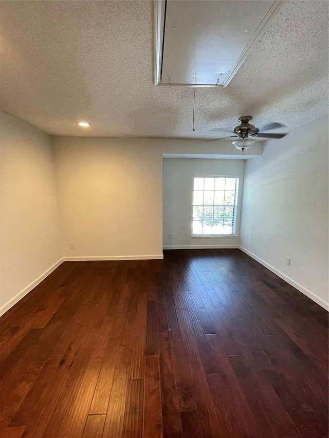 unfurnished room featuring baseboards, attic access, dark wood-style flooring, ceiling fan, and a textured ceiling