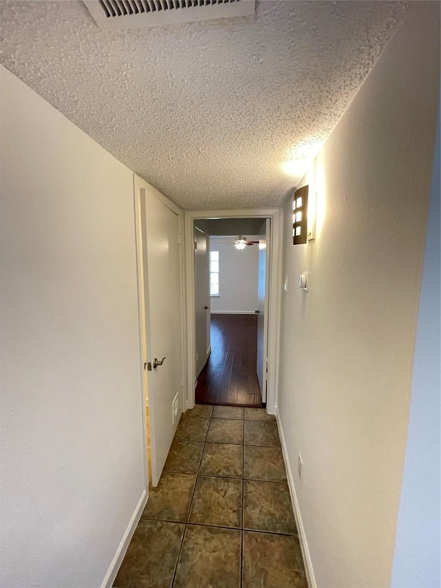 hall featuring tile patterned flooring, baseboards, visible vents, and a textured ceiling