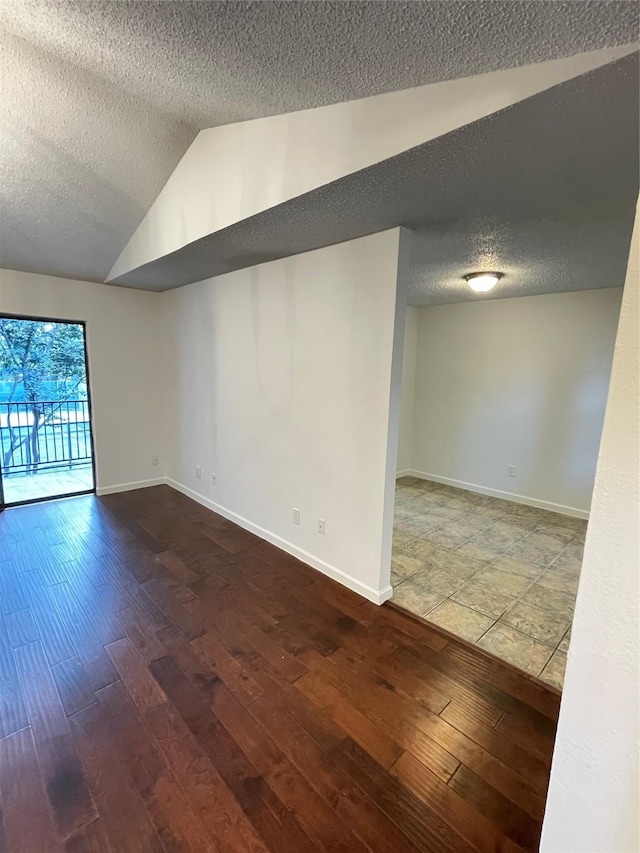 unfurnished room with baseboards, a textured ceiling, lofted ceiling, and wood finished floors