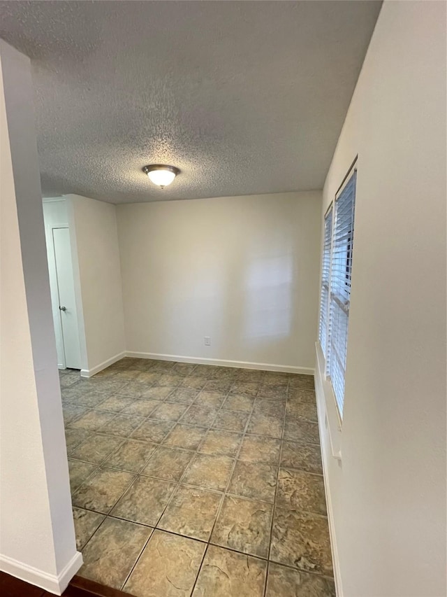 unfurnished room with baseboards and a textured ceiling