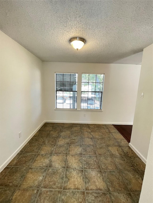 spare room featuring tile patterned flooring, a textured ceiling, and baseboards