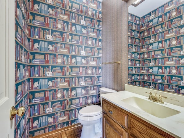 half bathroom featuring toilet, wallpapered walls, and vanity