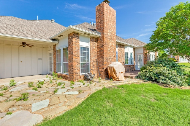 rear view of house featuring a chimney, a lawn, a shingled roof, brick siding, and a patio area
