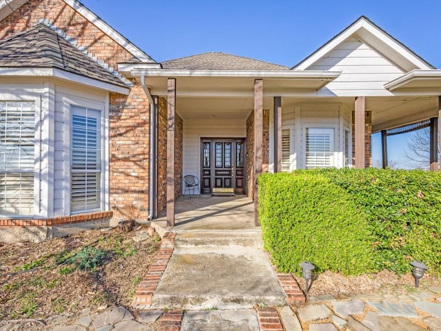 property entrance with brick siding, covered porch, and a shingled roof