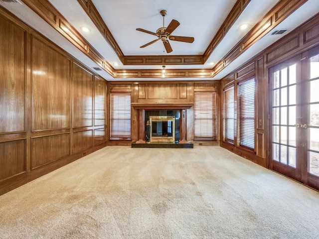 unfurnished living room with a high end fireplace, ornamental molding, ceiling fan, carpet floors, and a raised ceiling