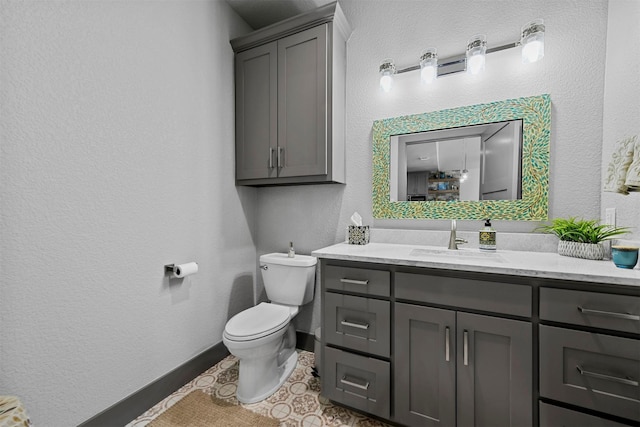 bathroom with toilet, vanity, baseboards, and a textured wall