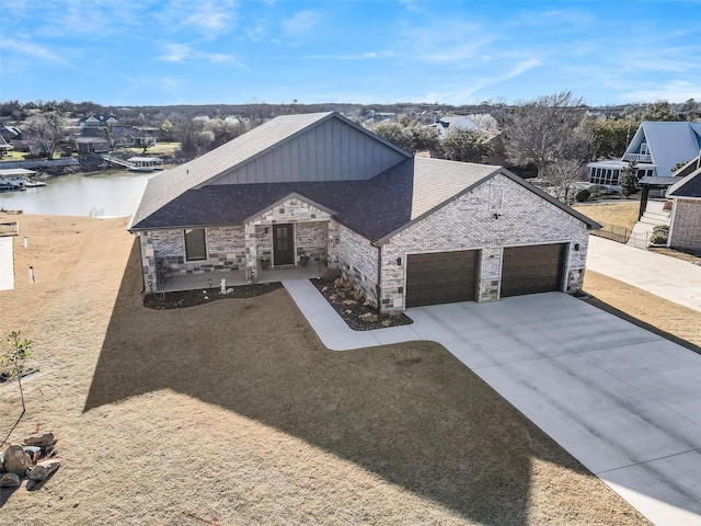 view of front facade with a water view, stone siding, concrete driveway, a shingled roof, and a garage