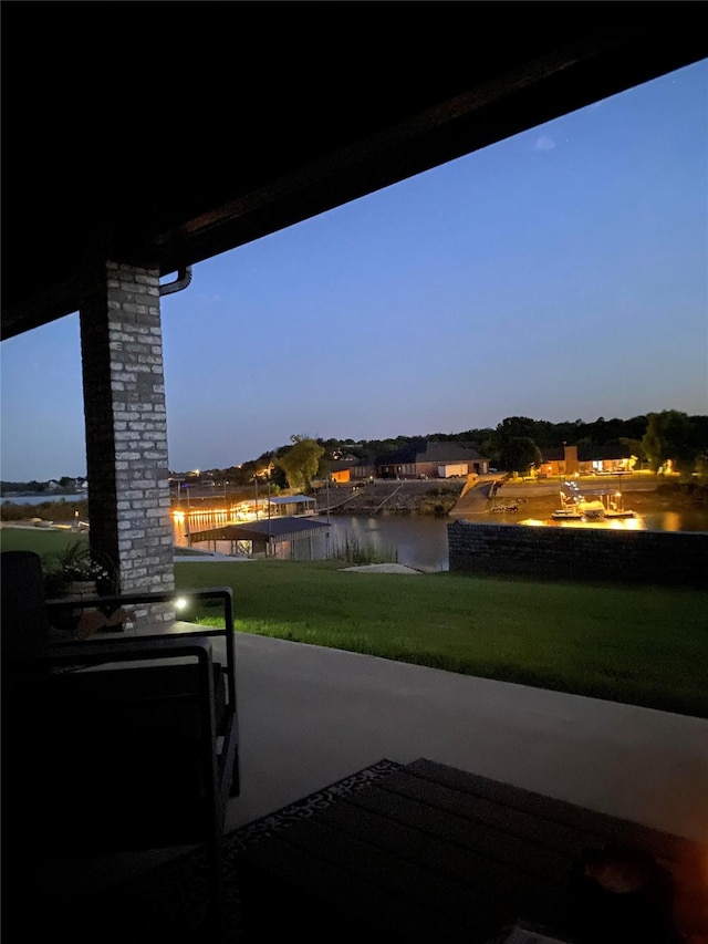 patio terrace at dusk featuring a water view and a lawn