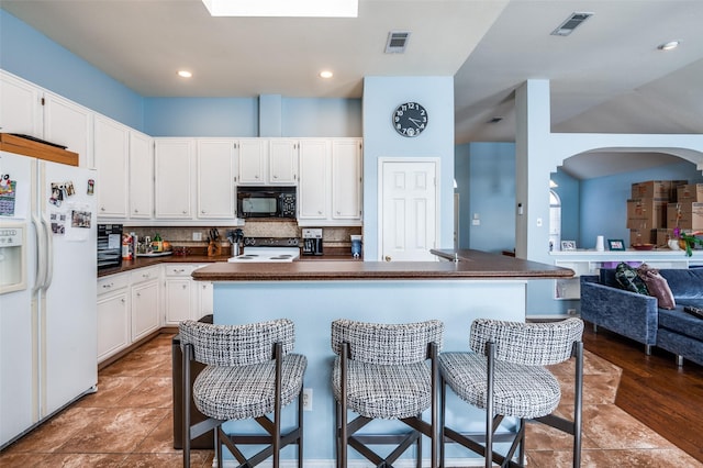 kitchen with dark countertops, visible vents, black microwave, and white fridge with ice dispenser