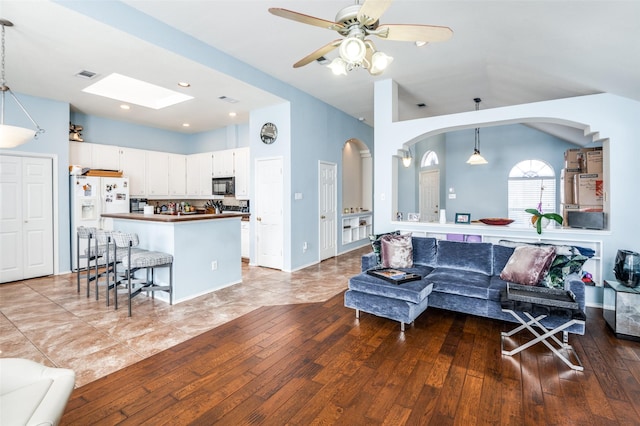 living area featuring hardwood / wood-style floors, a ceiling fan, visible vents, baseboards, and vaulted ceiling with skylight