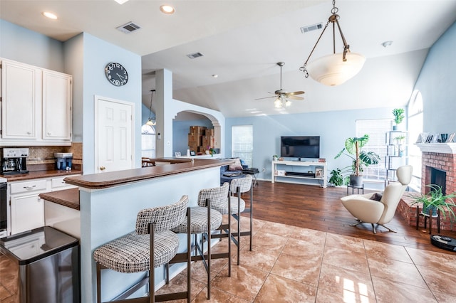 kitchen with dark countertops, visible vents, a fireplace, arched walkways, and white cabinets