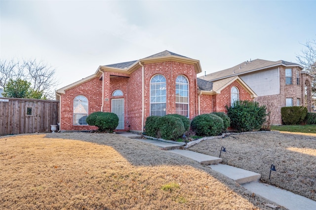 traditional home featuring brick siding, roof with shingles, a front yard, and fence