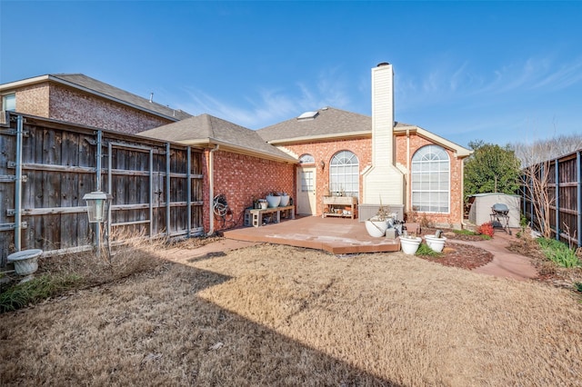 rear view of property featuring fence, brick siding, roof with shingles, and a chimney