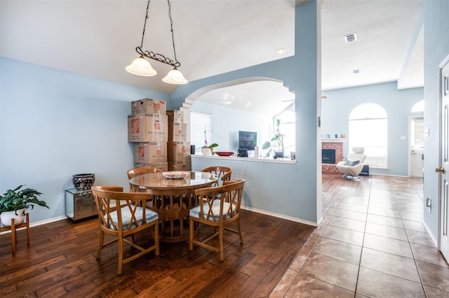 dining area with visible vents, wood finished floors, arched walkways, a fireplace, and baseboards