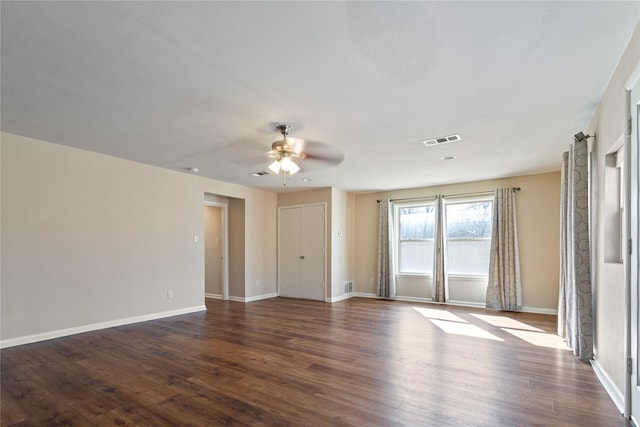 empty room with ceiling fan, visible vents, baseboards, and dark wood finished floors