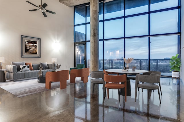 dining space with plenty of natural light, a ceiling fan, a wall of windows, and a high ceiling