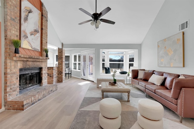 living room with visible vents, high vaulted ceiling, a brick fireplace, and light wood-style flooring