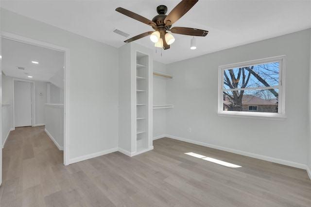 empty room with visible vents, ceiling fan, baseboards, built in features, and wood finished floors