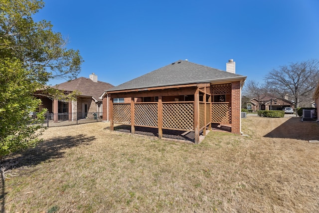 rear view of house featuring fence, a lawn, brick siding, and a chimney