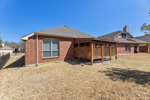 back of house with fence, a yard, roof with shingles, brick siding, and a chimney