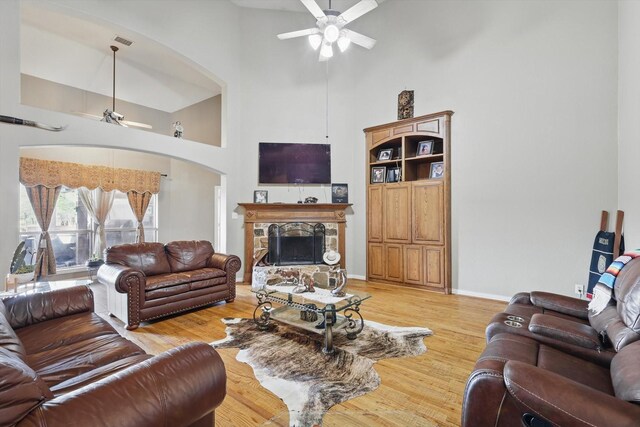 living area with light wood-type flooring, a high ceiling, a stone fireplace, and ceiling fan