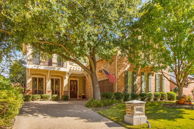 view of front of house with a front yard, a balcony, brick siding, and driveway