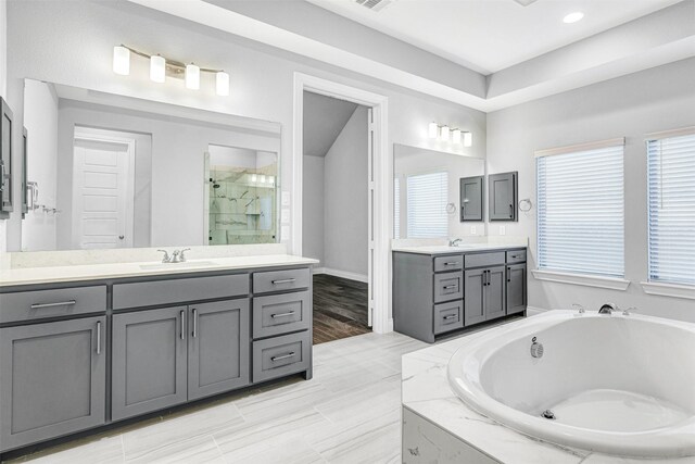 bathroom featuring visible vents, a garden tub, two vanities, a stall shower, and a sink