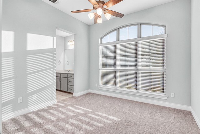 empty room featuring visible vents, light colored carpet, a ceiling fan, and baseboards