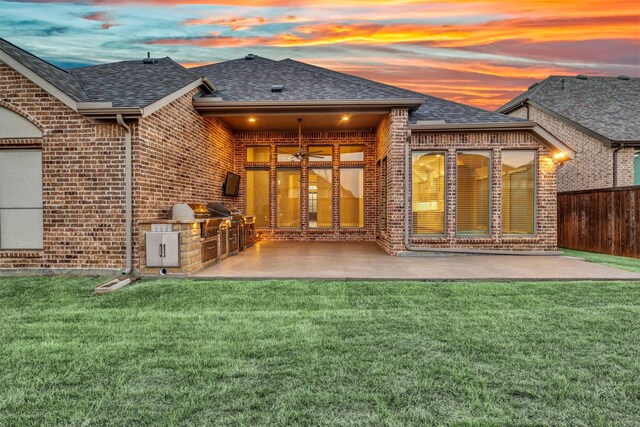 rear view of house with brick siding, roof with shingles, an outdoor kitchen, and fence