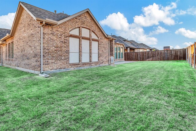 back of house with brick siding, roof with shingles, a fenced backyard, and a lawn