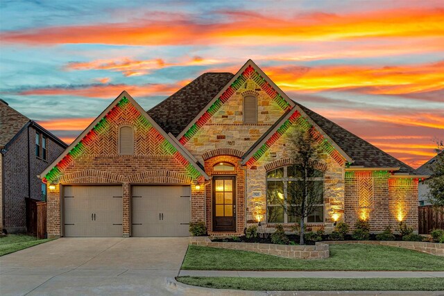 french country home with a garage, stone siding, brick siding, and driveway