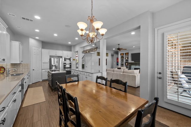 dining area featuring visible vents, a fireplace, recessed lighting, dark wood-style flooring, and ceiling fan with notable chandelier