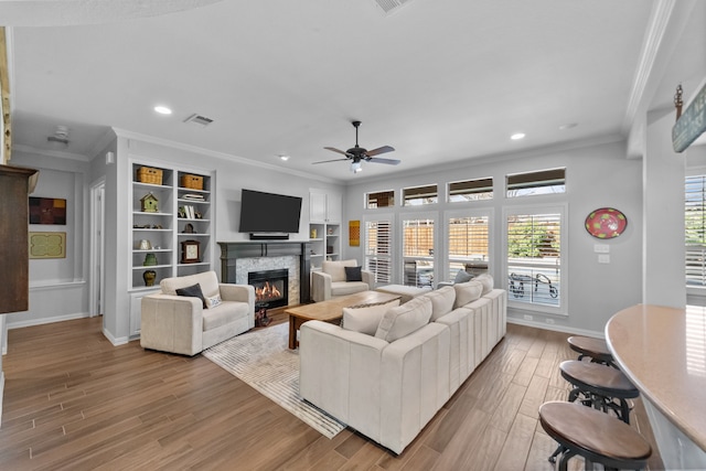 living area with visible vents, baseboards, ornamental molding, light wood-style flooring, and a fireplace