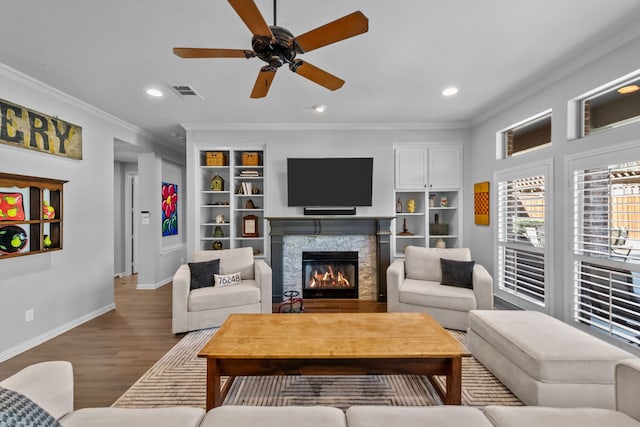 living room with wood finished floors, baseboards, visible vents, a fireplace, and crown molding