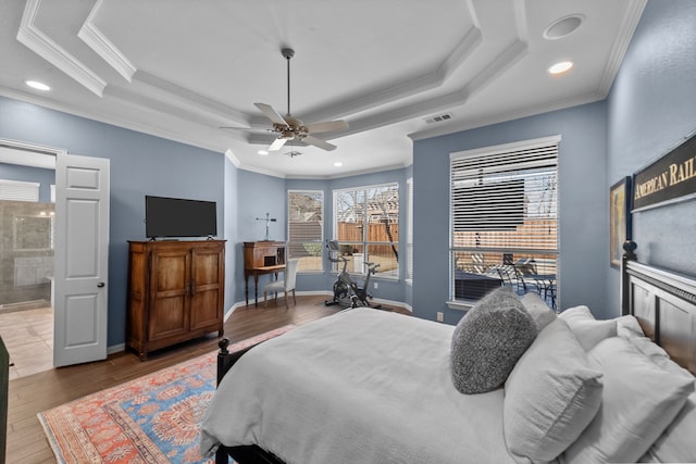 bedroom featuring visible vents, ornamental molding, a tray ceiling, wood finished floors, and baseboards