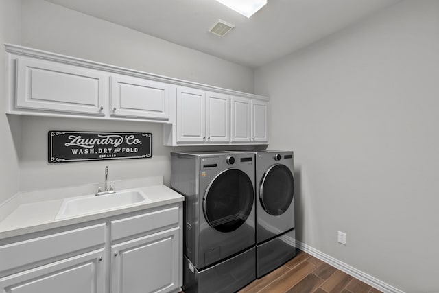 clothes washing area with visible vents, washer and clothes dryer, a sink, cabinet space, and wood tiled floor