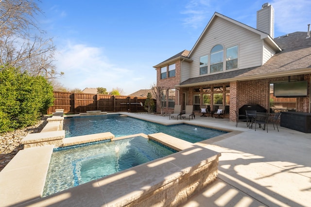 view of swimming pool with fence, a pool with connected hot tub, and a patio area