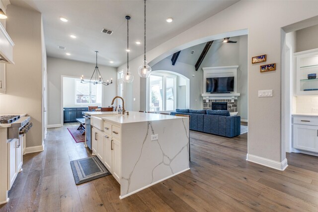 kitchen with visible vents, lofted ceiling with beams, white cabinetry, arched walkways, and a fireplace