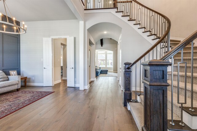 foyer with a notable chandelier, hardwood / wood-style floors, arched walkways, a towering ceiling, and stairs