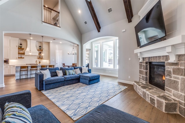 living room featuring a stone fireplace, beamed ceiling, light wood-style floors, and visible vents