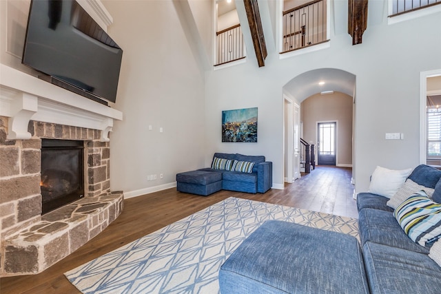 living room featuring stairs, a stone fireplace, wood finished floors, and a towering ceiling