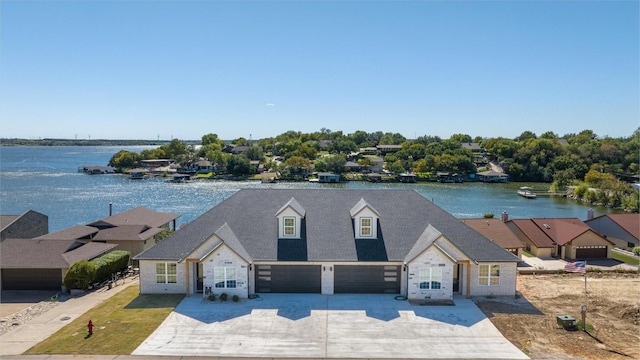 view of front of house with concrete driveway, a garage, a water view, and a shingled roof