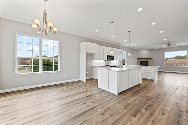 kitchen featuring a sink, stainless steel microwave, open floor plan, crown molding, and light wood finished floors